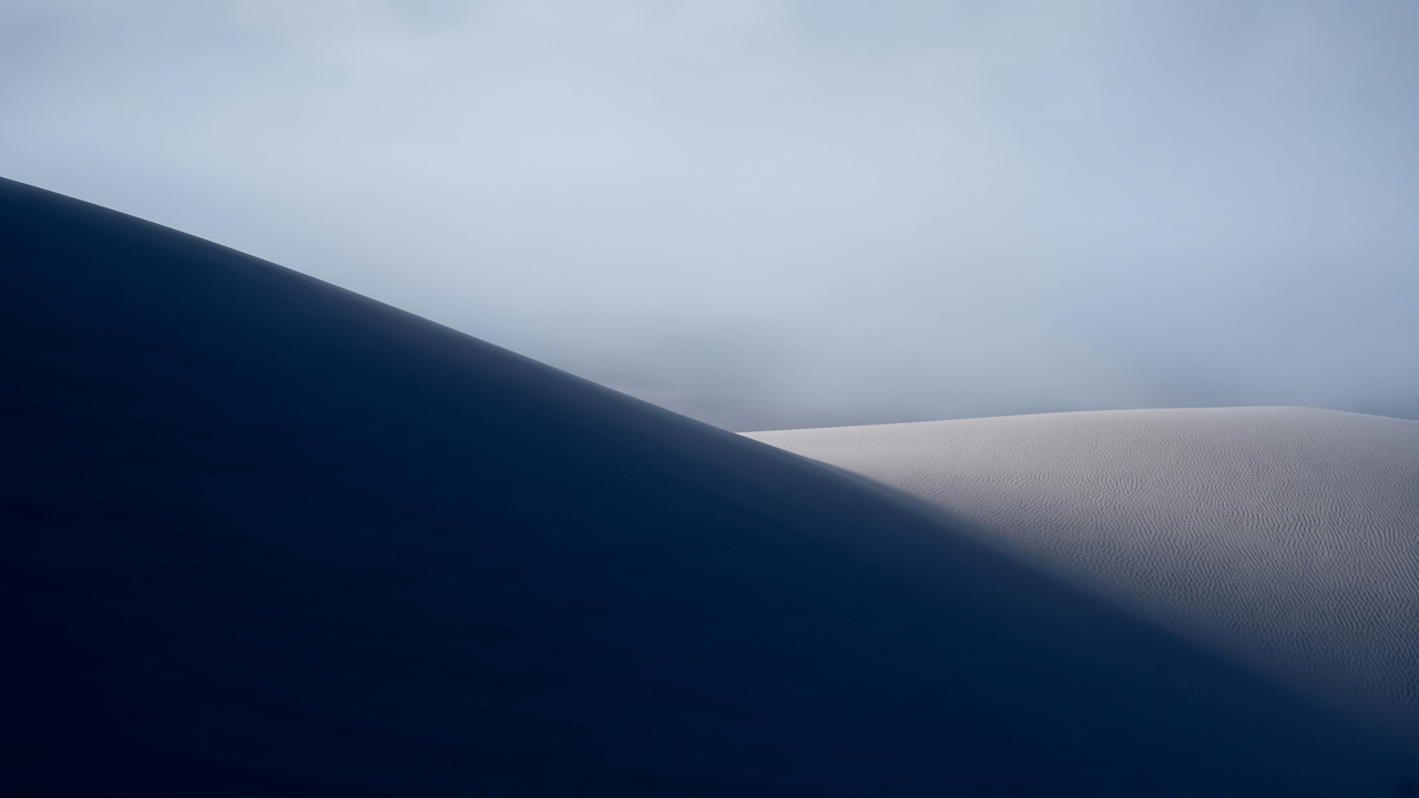 Dark navy dune slope in shadow beside a pale sunlit ridge in cool fog
