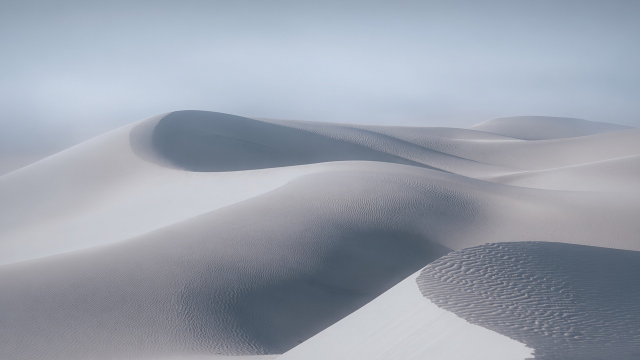 Smooth rounded dunes with faint parallel ripples in cool silver light