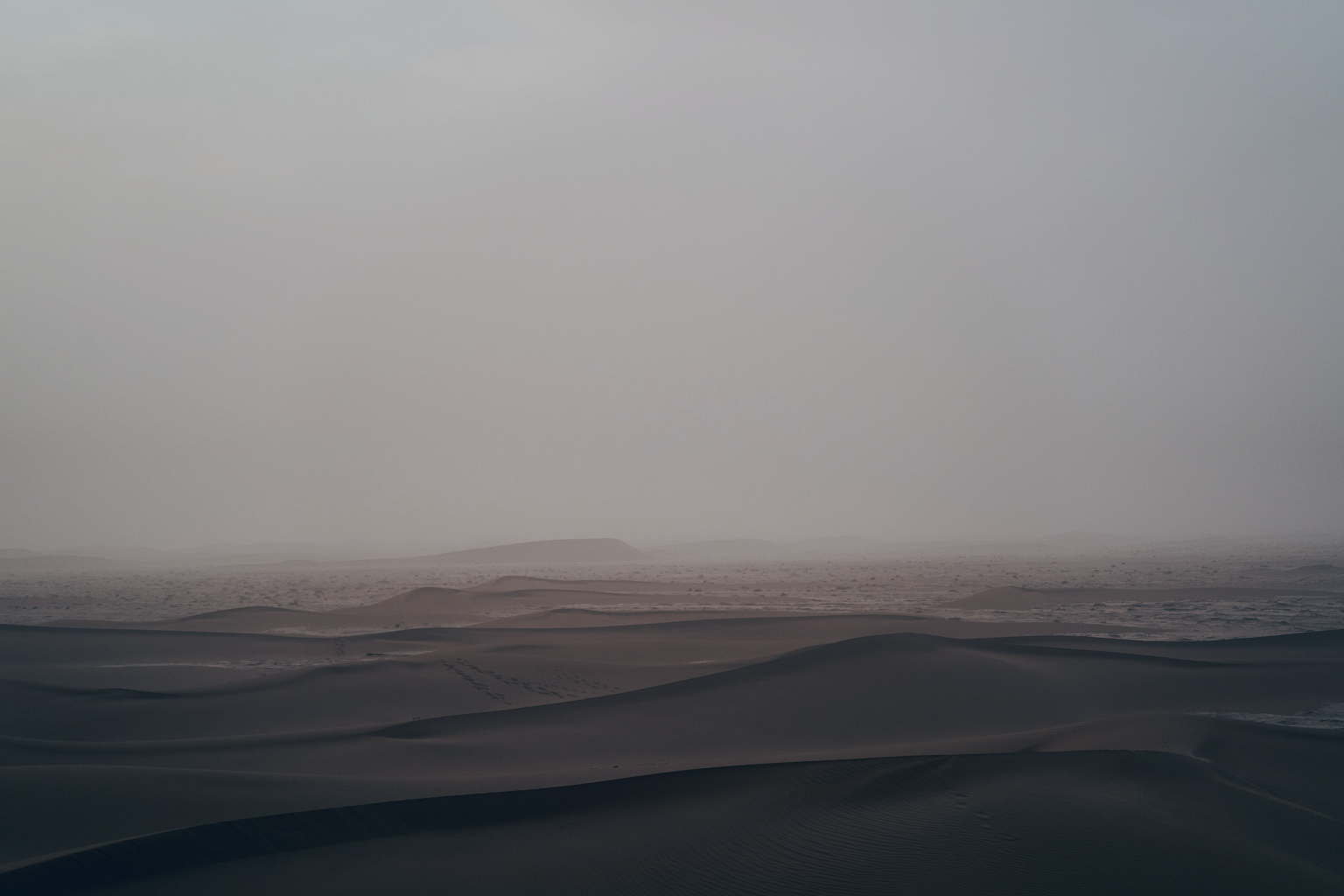 Low sand dunes receding into cool grey fog, soft ridgelines fading toward the horizon