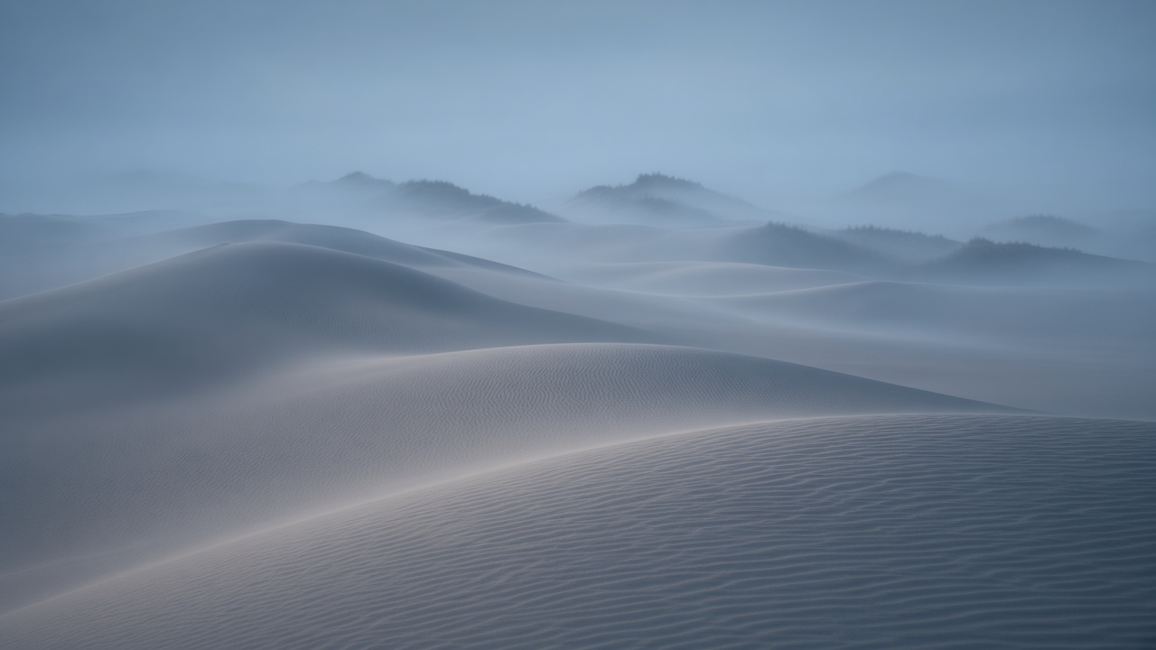 Distant dune ridgelines stacked in receding tones of blue and grey mist